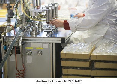 Manufacturing And Filling Perfume Bottles In A Factory. Cosmetics Production Conveyor Line In An Industrial Environment. A Lady In A White Laboratory Coat Working