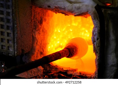 Manufacturing glass in a traditional oven, the glassblower working on a handmade vase of melted glass on a rod, selected focus and narrow depth of field - Powered by Shutterstock