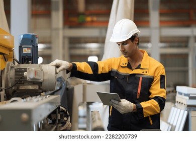 Manufacturing industrial in plant. Male engineer worker checking, repair and maintenance machine at manufacturing production lines in industry factory while wearing safety uniform, use digital tablet - Powered by Shutterstock