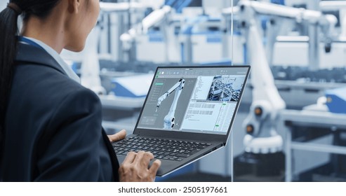 Manufacturing Robot Arms Administrator Programming Robotic Vision Systems to Execute Production at an Electronics Factory. Over the Shoulder Footage of a Female Supervising Assembly with a Computer