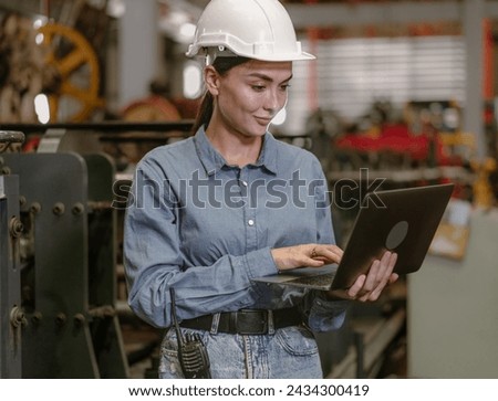 Manufacturing supervisor wear safety helmet examining heavy steel production in factory. Female engineer manager control product quality in workshop. Technician worker using laptop machine maintenance