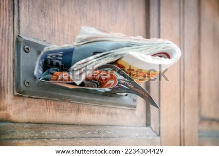 Many advertising leaflets are hanging from an overloaded letterbox. Closeup.