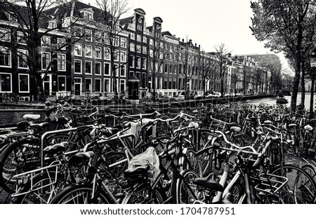 Many bicycles in the parking lot by the canal in Amsterdam. Black-white cityscape.