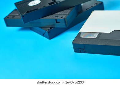 Many Black Old Vhs Video Cassette In White Cardboard Box On Blue Desk. Concept Of 90s. Copy Space