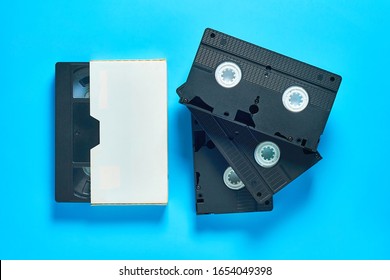 Many Black Old Vhs Video Cassette In White Cardboard Box On Blue Desk. Concept Of 90s. Top View. Close-up