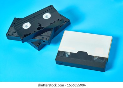 Many Black Old Vhs Video Cassette In White Cardboard Box On Blue Desk. Concept Of 90s. Close-up