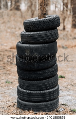 Many black round old used black car tires are put on a tree trunk in the forest. Photography, concept.