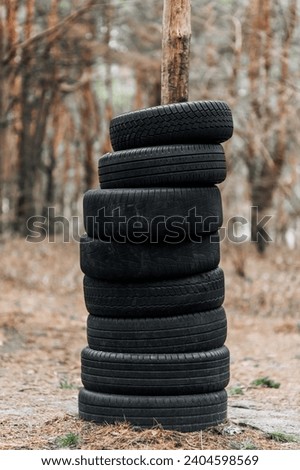 Many black round old used black car tires are put on top of a tree trunk in the forest in a row. Photography, concept.