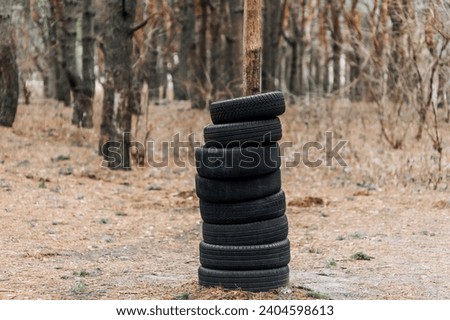 Many black round old used black car tires are put on a tree trunk in the forest in a row. Photography, concept.