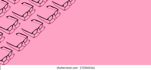 Many black trendy eyeglasses on pastel pink background. Repetitive pattern border frame. Minimal hipster eyewear concept. Copy space.