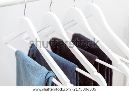 Many blue denim jeans hanging on white clothes hangers on clothing rack. Close up of folded casual denim jeans in wardrobe with coat hangers Foto stock © 