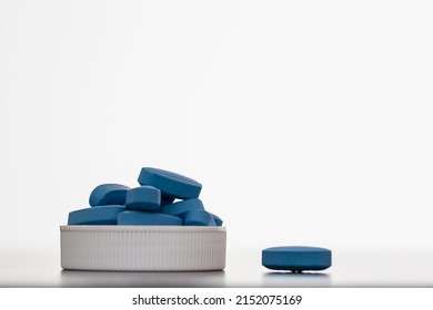 Many Blue Pills piled up in the lid and 1 single out on a white background; concept of using a medicine to solve a problem such as erectile dysfunction in men