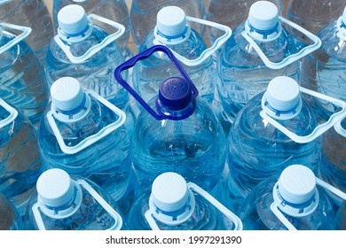 Many blue plastic bottles with blue caps and one with dark blue cap with clear mineral water in a supermarket. Pure filtered ecologically clean water in packaging. Close Up. One is different from all