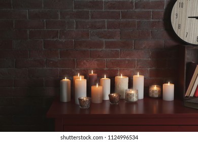 Many burning candles on wooden table against brick wall - Shutterstock ID 1124996534