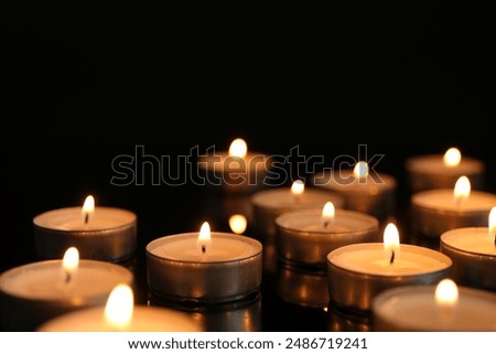 Many burning tealight candles on black background, closeup