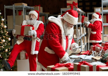 Many busy Santa Clauses packing gift boxes preparing fast xmas delivery. Three funny Santas walking in workshop warehouse in Merry Christmas rush delivering presents during holiday preparations.