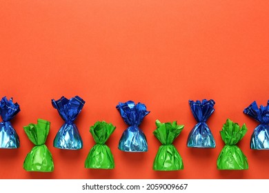 Many candies in colorful wrappers on orange background, flat lay. Space for text