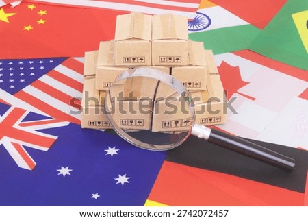 Many cardboard boxes on different national flags under magnifying glass. Global trading, shipping and tariffs concept.