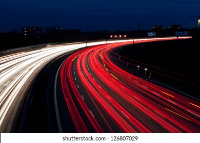 many cars are driving at night on a highway and create light trails.