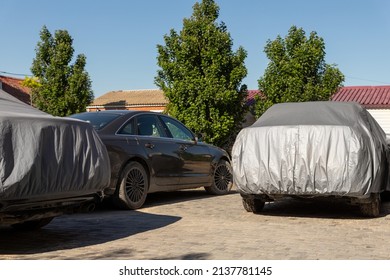 Many Cars Parked Near Suburban Home Driveway Covered With Protective Tarpaulin Cloth Cover To Protect From Direct Sun Light, Dust, Rain Or Hail On Hot Summer Day. Vehicle Care And Safety Protetction