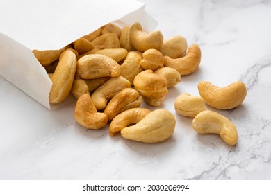 Many Cashew Nuts On Marble Background Out Of White Paper Packet. Source Of Natural Fats And Protein. Healthy Eating Or Diet Concept.