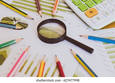 Many charts and graphs with pencil, magnifying glass, calculator, clock. Reflection light and flare. Concept image of data gathering and statistical working.
