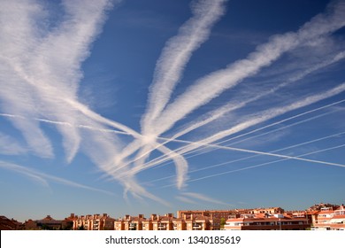 Many chemtrails or contrails produced by airplanes flying on blue sky over the city	