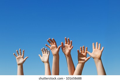 Many children hands raised up against the blue sky with copy space