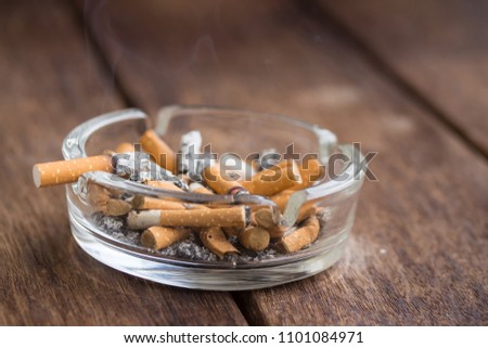 Many cigarette stubs and ash in a glass ashtray on wooden table
