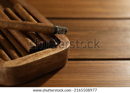 Many cigars in box on wooden table, closeup. Space for text