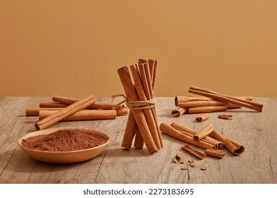 Many cinnamon sticks are decorated on a wooden table with cinnamon powder placed on a dish. Cinnamon (Cinnamomum) brings a lot of benefits for health, body and skin - Shutterstock ID 2273183695