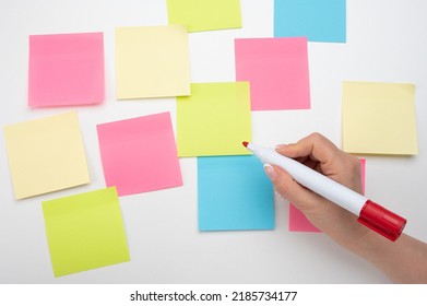 Many Colored Empty Sticker Notes On White Wall. Hand With Red Marker Ready To Write. Blank Sticker Notes On White Background. Mockup Sticky Note Paper. Empty Sheets For Notes On White Bulletin Board