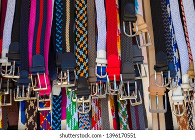 Many colorful belts with silver belt buckles hang on a Spanish weekly market at a stall next to each other. - Shutterstock ID 1396170551