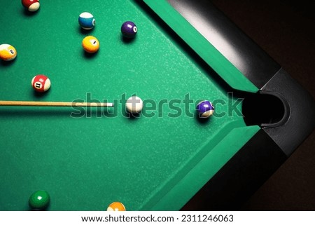 Many colorful billiard balls and cue on green table, top view