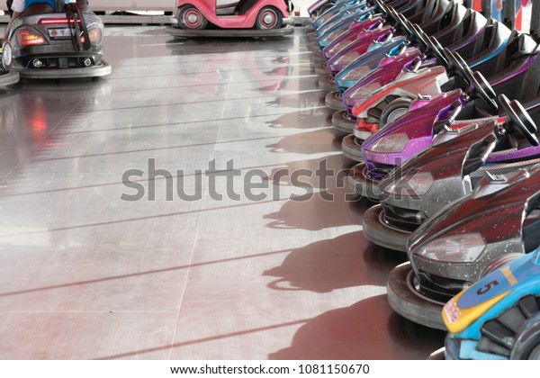 Many colorful bumper cars parked at amusement\
park with some of them being ride. Shadow of bumper cars from\
sunlight provided as room for\
text.