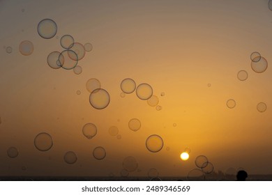 Many colorful soap bubbles float in the orange sky at sunset