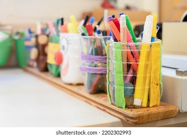 Many coloring pens and pencils in pencil holders on worktable in art class, studio or school. Arts and craft background texture. DIY project  or kids crafts and creative activities. Selective focus.