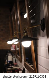 Many Copper Lamp Sconce Hanging From White Tile Wall Near Big Mirrors In Beauty Salon.