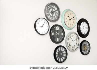 Many Different Clocks Hanging On White Wall.