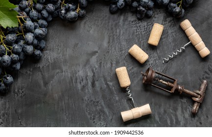 Many Different Corkscrews With Open Wine Corks On Dark Concrete Background In Frame Made Of Black Grapes. Degustation Winetasting Of Wines Drink. Wine Bar Restaurant. Long Web Banner With Copy Space