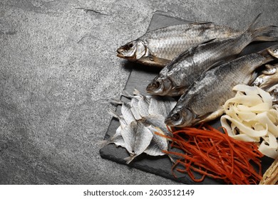 Many different dried fish snacks on grey table. Space for text