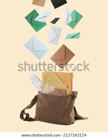 Many different envelopes falling into brown postman's bag on beige background