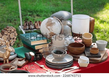 Many different items on red tablecloth outdoors. Garage sale