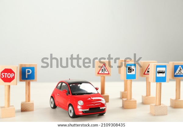 Many different miniature road\
signs and car on white wooden table, space for text. Driving\
school