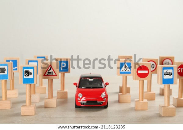 Many different miniature road signs\
and car on wooden table, space for text. Driving\
school