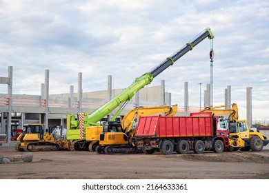 Many different multiclored colorful heavy industrial machinery equipment at construction site parking area against warehouse building city infrastructure development. Commercial vehicles rental sale.