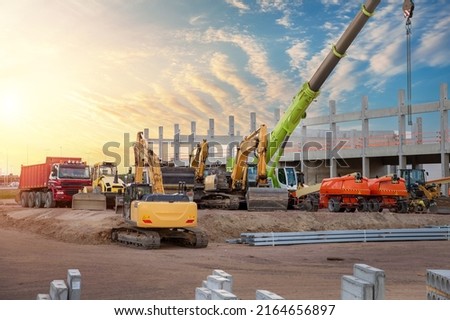 Many different multiclored colorful heavy industrial machinery equipment at construction site parking area against warehouse building city infrastructure development. Commercial vehicles rental sale