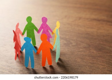 Many different paper human figures standing in circle on wooden table, space for text. Diversity and inclusion concept - Powered by Shutterstock