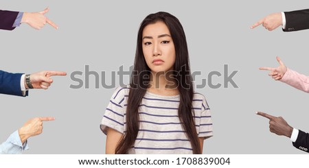 Many different people hands are pointing on guilty alone young brunette woman and blame her. she looking at camera with sad face. indoor studio shot, isolated on gray background.