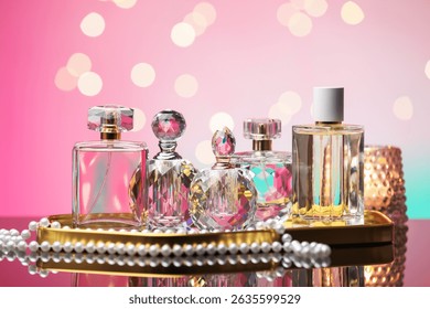 Many different perfume bottles and accessories on mirror surface against pink background with blurred lights, closeup